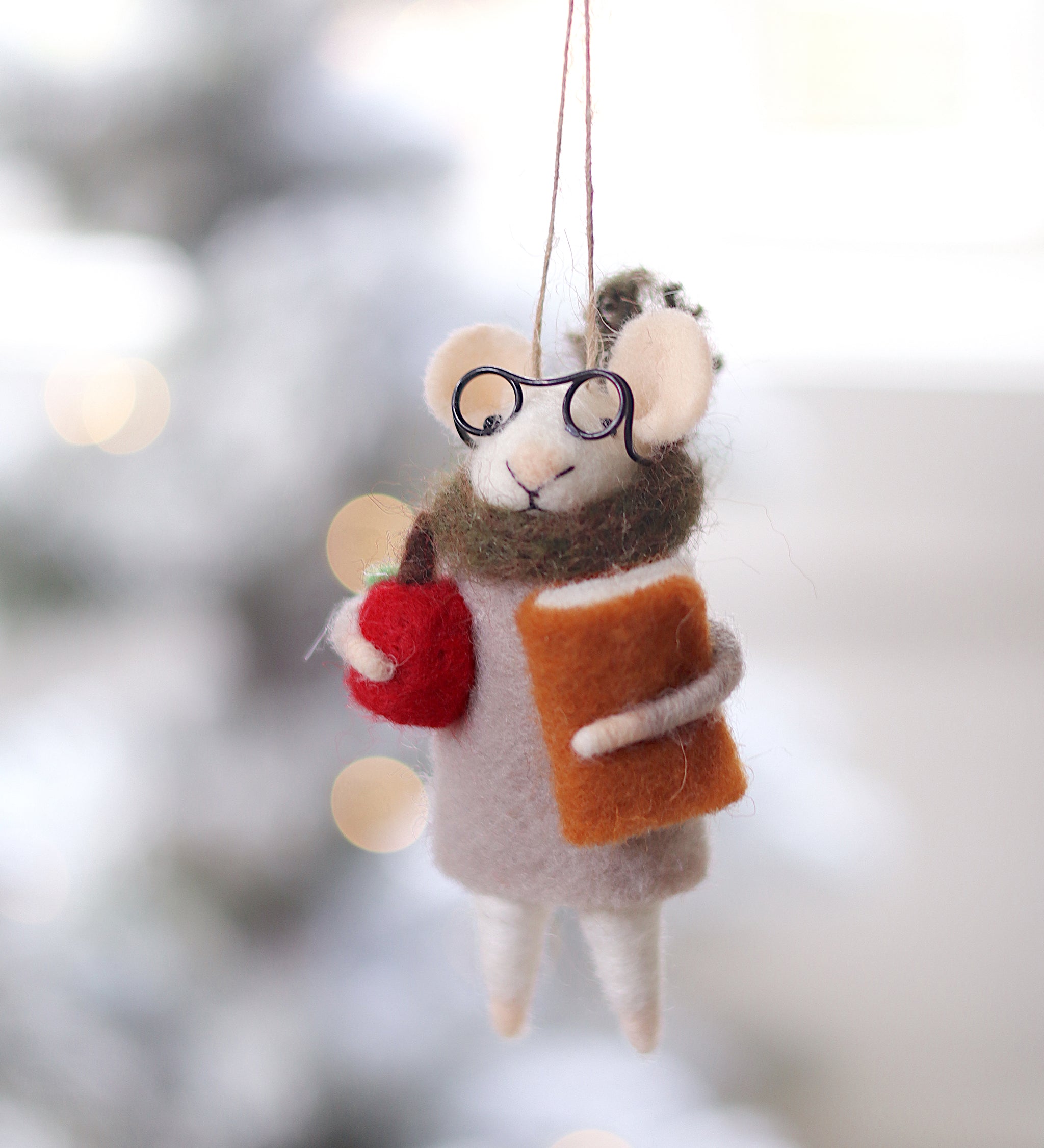 Decorative mouse ornament with glasses and a book, hanging against a blurred festive background. Available at Be Charmed
