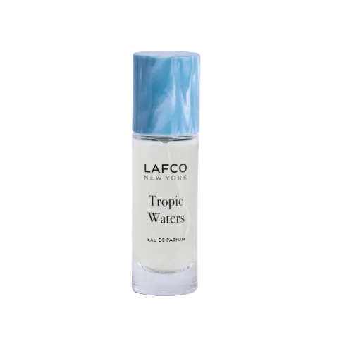 A bottle of LAFCO New York Tropic Waters Eau de Parfum with a light blue marbled cap and a clear glass body showing the white liquid inside, set against a plain white background. Available at Be Charmed