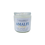 A 7.5 oz soy candle jar with a label reading 'Amalfi Breeze' and indicating the scent with lemon, bergamot, and mint. Available at Be Charmed