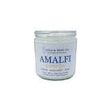 A 7.5 oz soy candle jar with a label reading 'Amalfi Breeze' and indicating the scent with lemon, bergamot, and mint. Available at Be Charmed