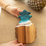 Wooden ocean vibes pineapple-shaped cutting board with a blue resin top held by a person on a beige surface. Availabe at Be Charmed