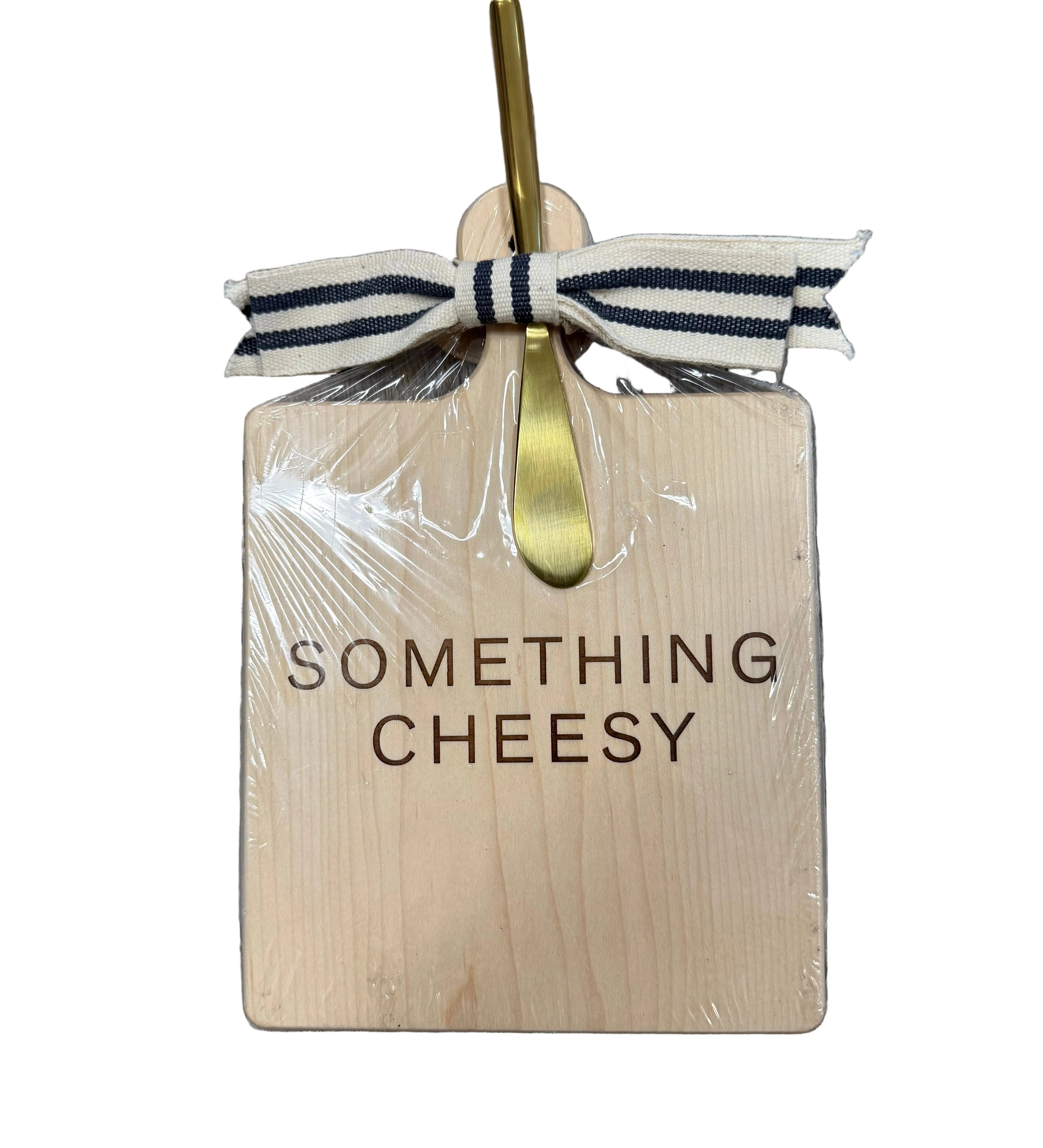 Wooden cutting board with 'Something Cheesy' text, gold fork, and ribbon on a wooden surface. Available at Be Charmed