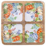 A square wooden Boston International serving board or tray holding four square ceramic coasters. The coasters feature a white background with an autumn floral and pumpkin pattern in orange, blue, green, and cream tones. Available at Be Charmed