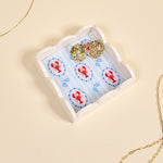 Gold earrings on a decorative tray with lobster design on a beige background. Available at Be Charmed