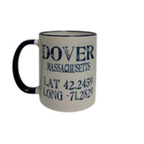 A white ceramic coffee mug with a navy handle and navy rim, printed with the text 'DOVER MASSACHUSETTS' and coordinates in dark blue lettering. Available at Be Charmed