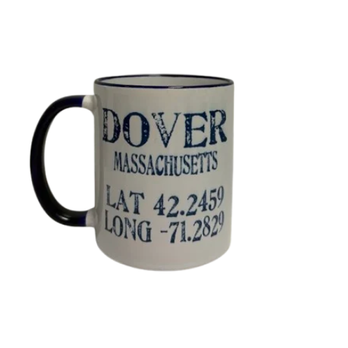 A white ceramic coffee mug with a navy handle and navy rim, printed with the text 'DOVER MASSACHUSETTS' and coordinates in dark blue lettering. Available at Be Charmed