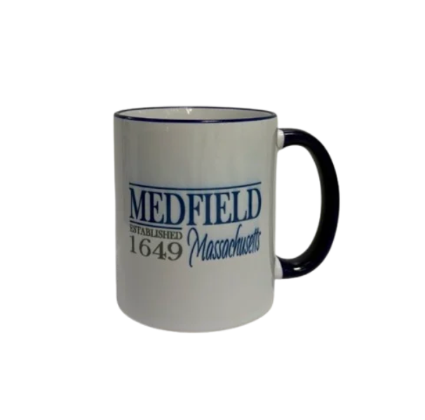 A white ceramic coffee mug with a navy handle and rim, featuring the text 'MEDFIELD ESTABLISHED 1649 Massachusetts' printed in navy blue and gray on the side. Available at Be Charmed