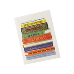 A birthday greeting card featuring a stack of colorful illustrated books with text including 'HERE'S TO ANOTHER Card Charlotte', 'HAPPY BIRTHDAY', and a quote from Mary Anne Patterson, shown on a light gray background. Available at Be Charmed