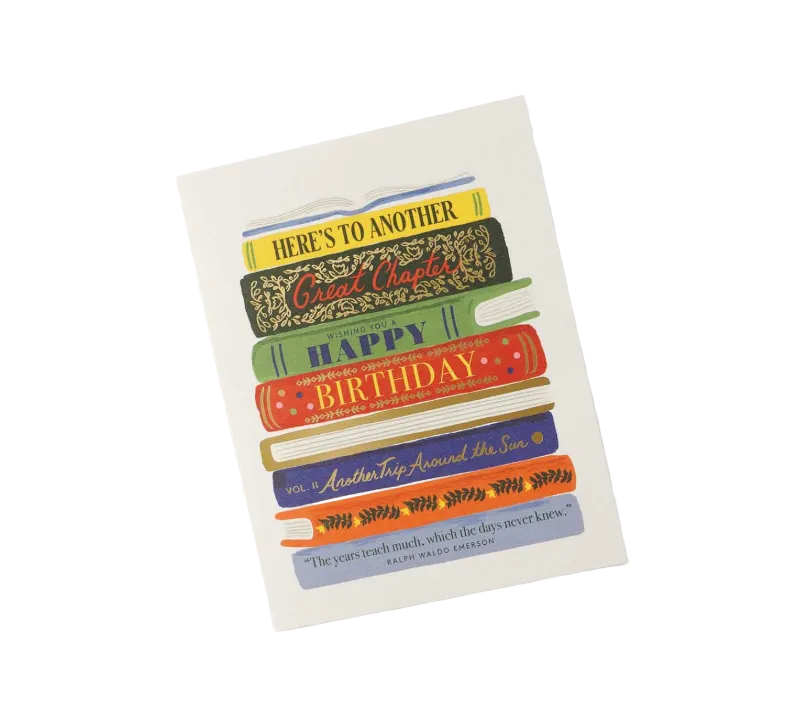 A birthday greeting card featuring a stack of colorful illustrated books with text including 'HERE'S TO ANOTHER Card Charlotte', 'HAPPY BIRTHDAY', and a quote from Mary Anne Patterson, shown on a light gray background. Available at Be Charmed