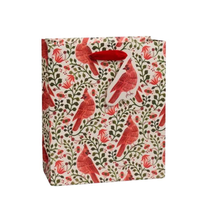 A Rifle Paper Co gift bag with a repeating pattern of red cardinals, green leaves, and small red flowers on a cream background, featuring red paper handles.  Available at Be Charmed