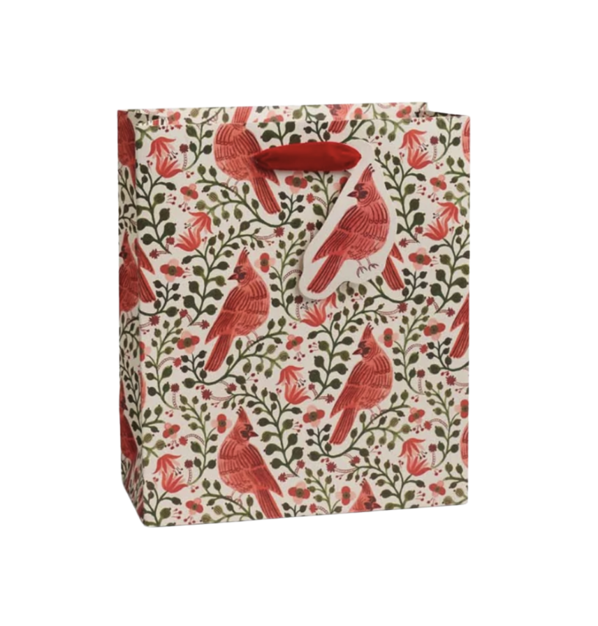 A Rifle Paper Co gift bag with a repeating pattern of red cardinals, green leaves, and small red flowers on a cream background, featuring red paper handles.  Available at Be Charmed