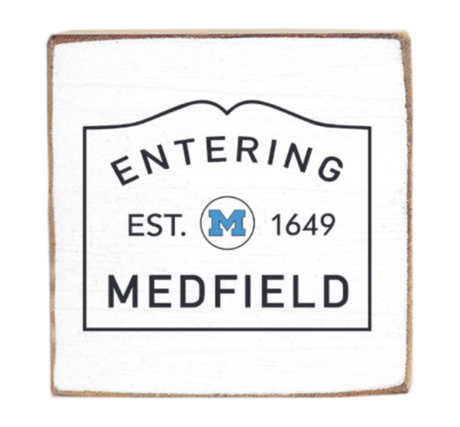 Decorative wooden block with 'Entering Medfield' text and a logo on a white background. Available at Be Charmed
