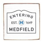 Decorative wooden block with 'Entering Medfield' text and a logo on a white background. Available at Be Charmed