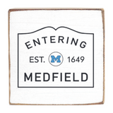 Decorative wooden block with 'Entering Medfield' text and a logo on a white background. Available at Be Charmed