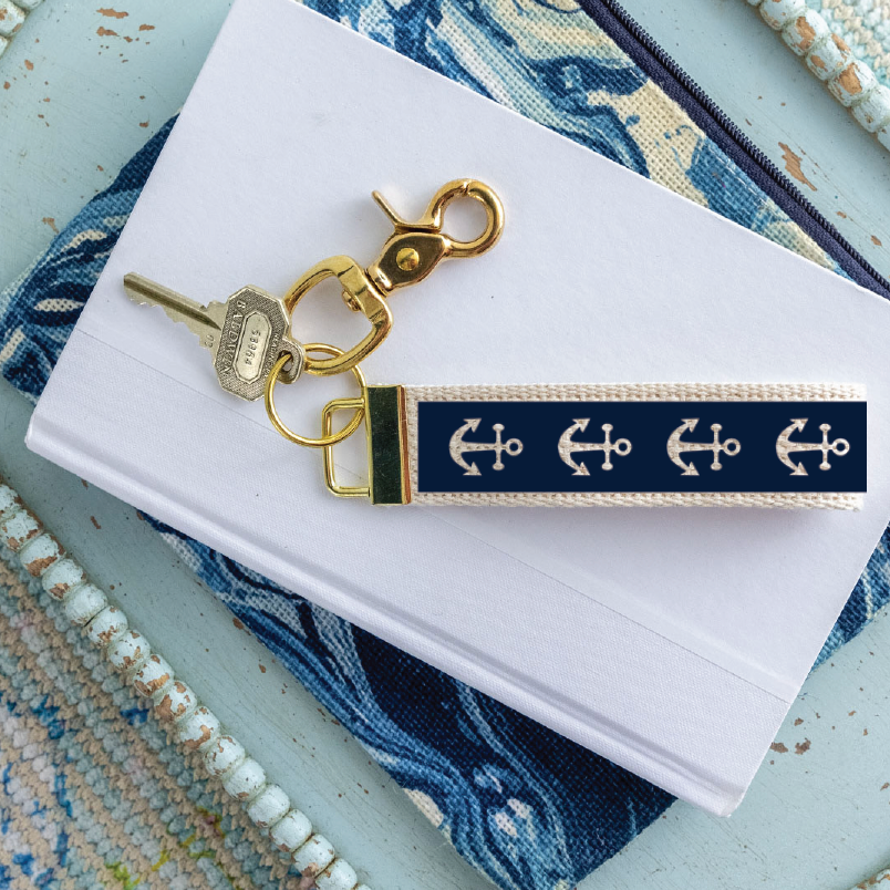 Gold keychain with navy strap featuring white anchors on a white card with blue floral design. Available at Be Charmed