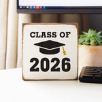 Decorative block with 'Class of 2026' text on a desk with a computer and plant in the background. Available at Be Chamed
