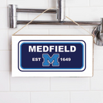 A rectangular wooden sign with 'MEDFIELD EST. 1649' printed in blue and white, hanging on a shower wall. Available at Be Charmed