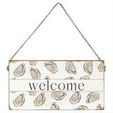 Decorative 'welcome' sign with oyster shell pattern on a white background. Available at Be Charmed