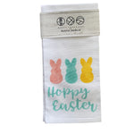 A rustic style tea towel with 'Happy Easter' text and decorative bunny illustrations in multicolor on a white background. Available at Be Charmed