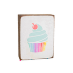 A decorative wooden block with a cupcake design, featuring a multicolored icing and a cherry on top, placed on a surface with colorful sprinkles scattered around. Available at Be Charmed