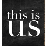 A black and white wood block sign with the text 'This Is Us' in the center. Available at Be Charmed