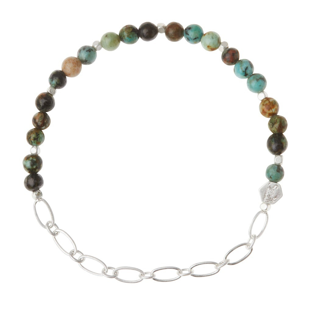 A mini chain bracelet with African turquoise beads, a silver chain, and an engraved hexagon Scout logo bead. Available at Be Charmed