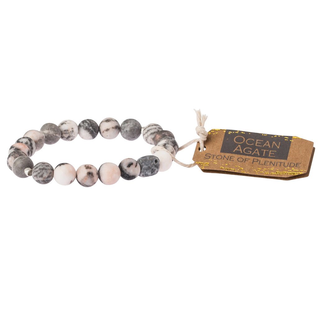 A grey stone stacking bracelet with a label tagged 'stone of plentitude'. Available at Be Charmed