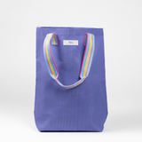 A purple woven Scout tote bag with a multicolored striped handle. Available at Be Charmed