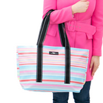A woman holding a multi striped Scout tote bag with black straps and a front brand label. Available at Be Charmed