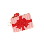 A small zippered Darling Effect pouch designed to look like a wrapped gift box, featuring a pink and white striped body with a red beaded bow on the front, a red pull tab, and a gold-tone key ring. Available at Be Charmed