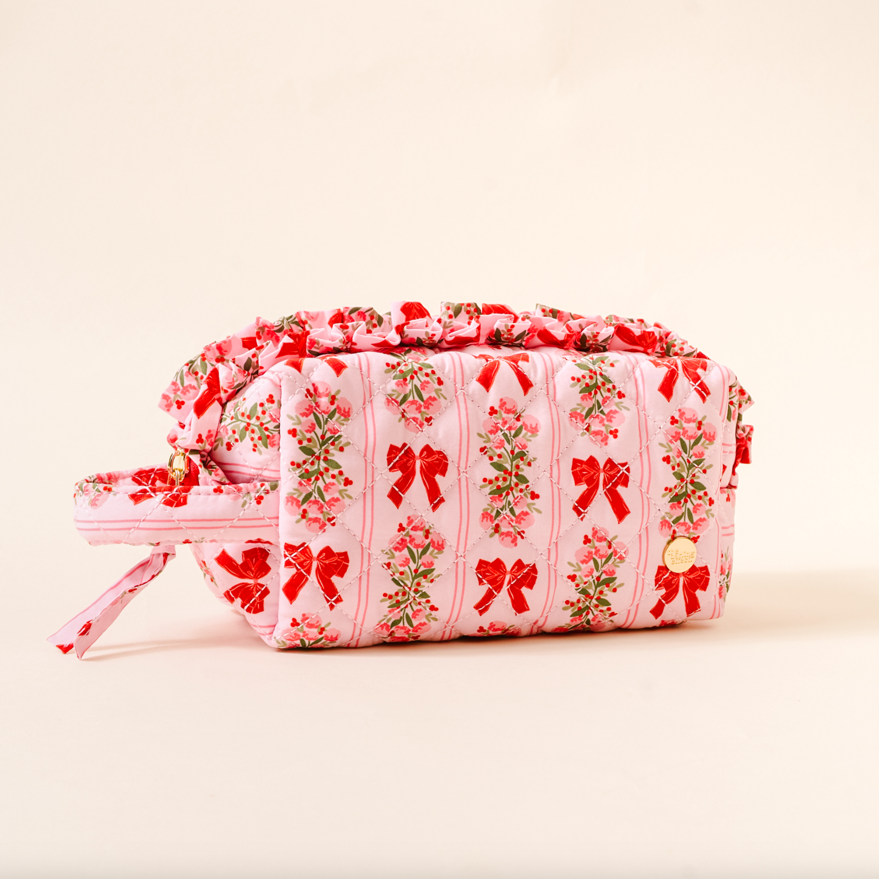 Pink cosmetic bag with floral and bow pattern on a beige background. Available at Be Charmed. 
