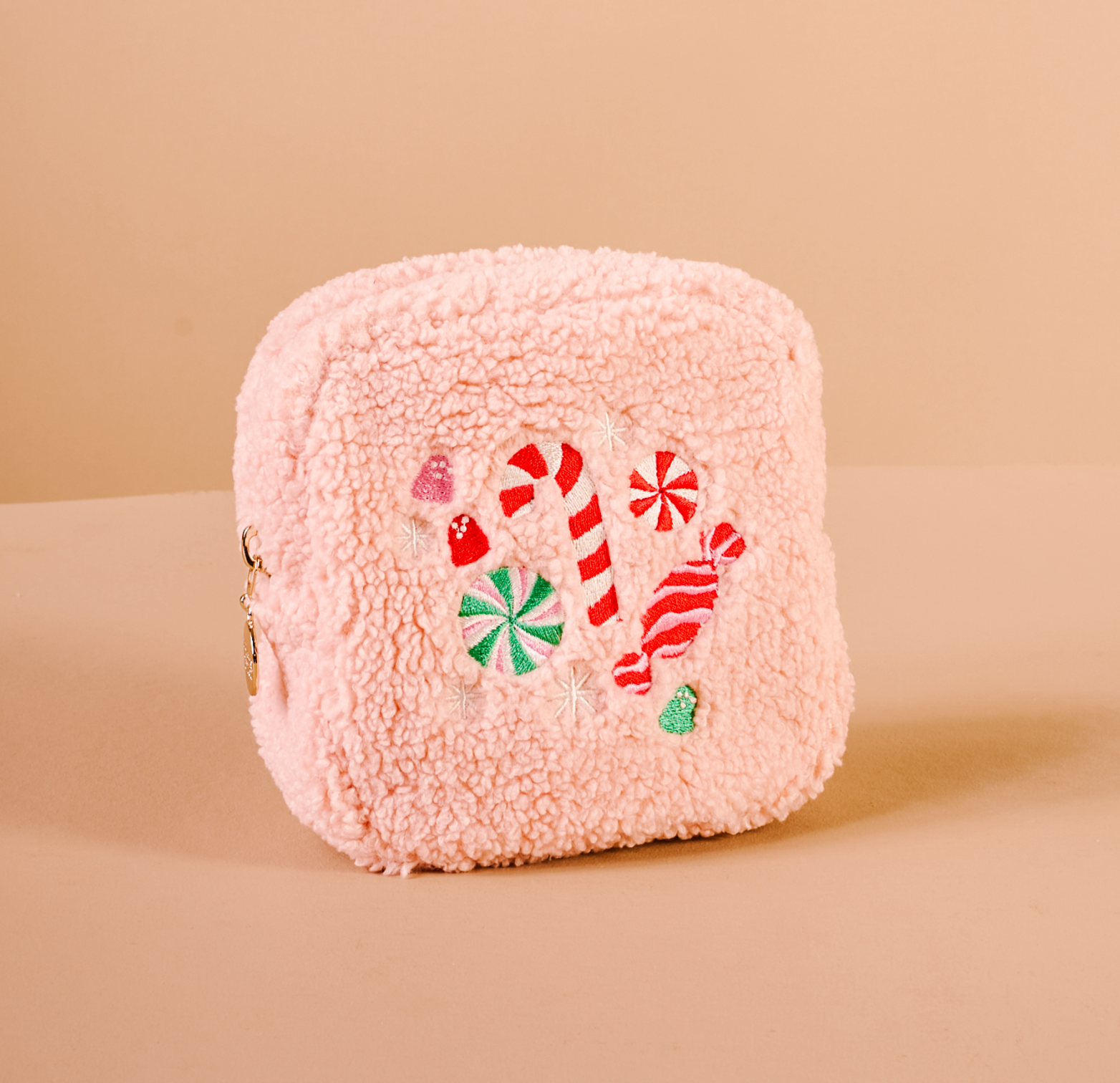 Pink fluffy cosmetic pouch with candy-themed design on a beige background. Available at Be Charmed.