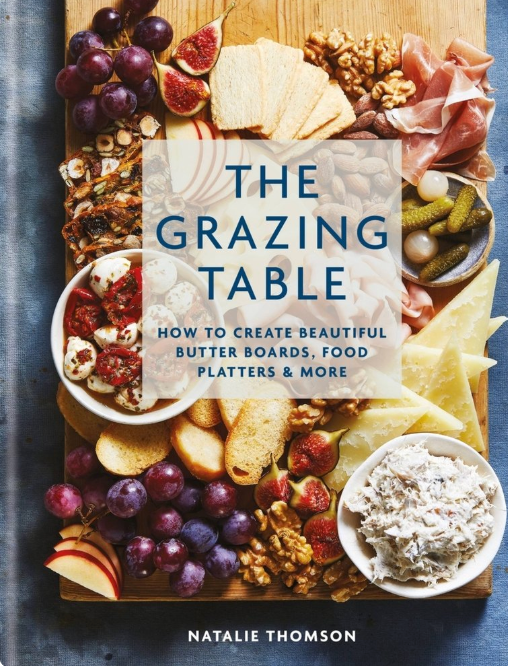 Book cover of 'The Grazing Table' with a wooden board filled with food items on a blue background. Available at Be Charmed