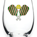 A clear stemless wine glass featuring a decorative front emblem of two crossed pickleball rackets with green and pink striped wings, a yellow textured center, and silver crossed handles, shown on a white background. Available at Be Charmed