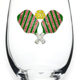 A clear stemless wine glass featuring a decorative front emblem of two crossed pickleball rackets with green and pink striped wings, a yellow textured center, and silver crossed handles, shown on a white background. Available at Be Charmed