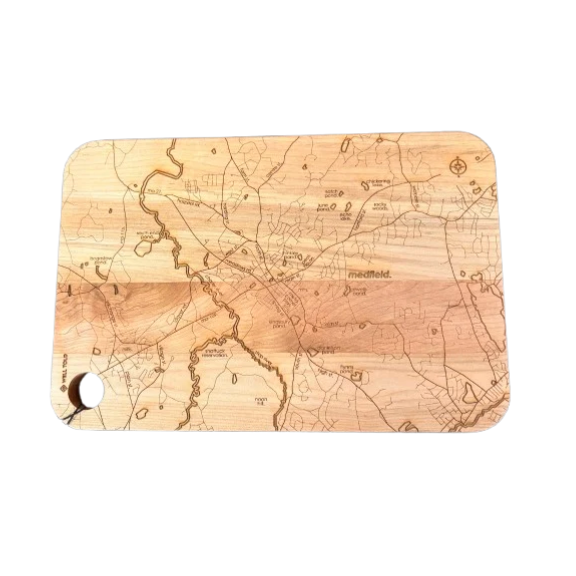 A Well Told rectangular wooden cutting board with rounded corners, featuring an engraved topographic map design in light and dark brown tones, and a hanging hole on the bottom left, shown against a plain white background. Available at Be Charmed